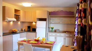A modern kitchen with wooden cabinets, a dining table set for two, and a refrigerator.