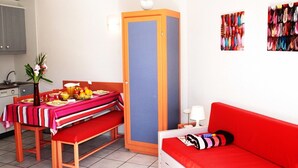 A compact room with a dining table set for two, a red sofa, a tall cabinet, and a wall with colorful artwork.