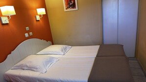 A double bed with white and brown bedding, two wall-mounted lamps, a small statue, and a closed door.