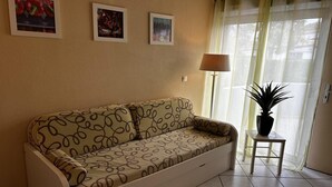 A living room with a sofa, a small table with a plant, and three framed pictures on the wall.