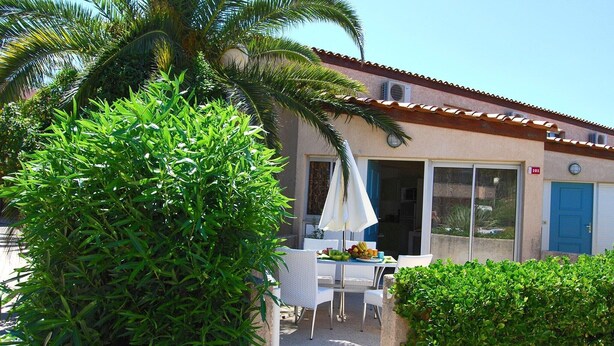 Une terrasse avec une table et des chaises, un palmier et un bâtiment avec une porte bleue.