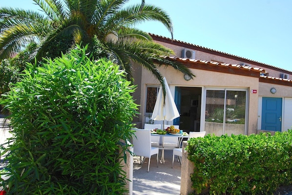 Une terrasse avec une table et des chaises, un palmier et un bâtiment avec une porte bleue.