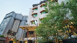 A multi-story building with balconies, a decorative facade, and a tree in the foreground. - Treebo Vice President (Ahmedabad)