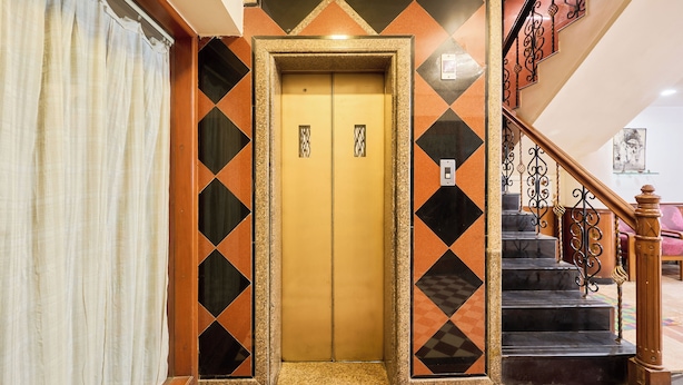An elevator with a geometric patterned wall, a staircase with a metal railing, and a tiled floor. - Treebo Vice President (Ahmedabad)