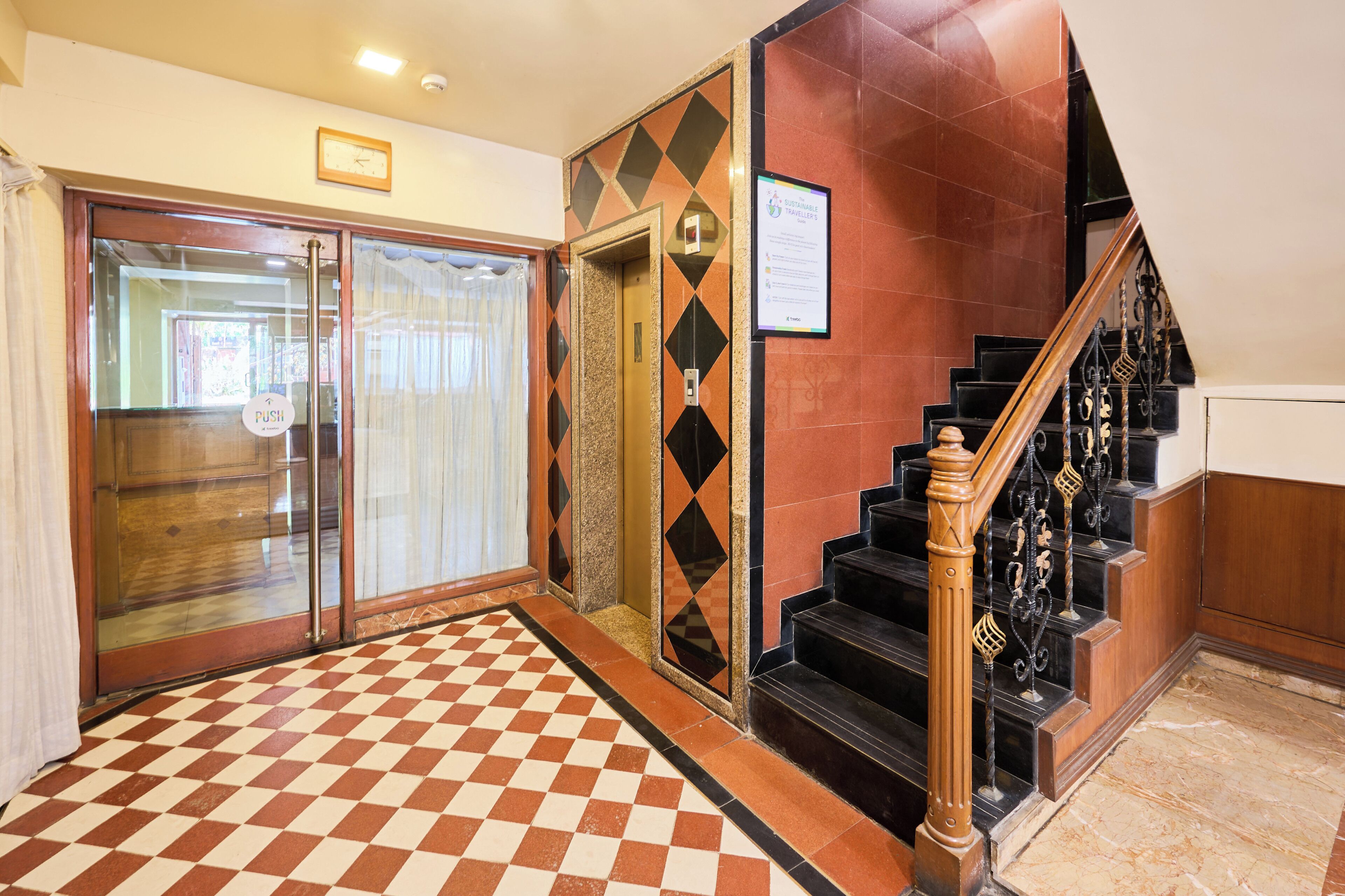 A hotel lobby with a checkered floor, a staircase with ornate railings, and a 'PUSH' sign on the door.