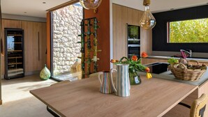 A modern kitchen with a wooden island, a stone wall, and a window with a view. - Contemporary villa with views of Cap d'Antibes (Nice)