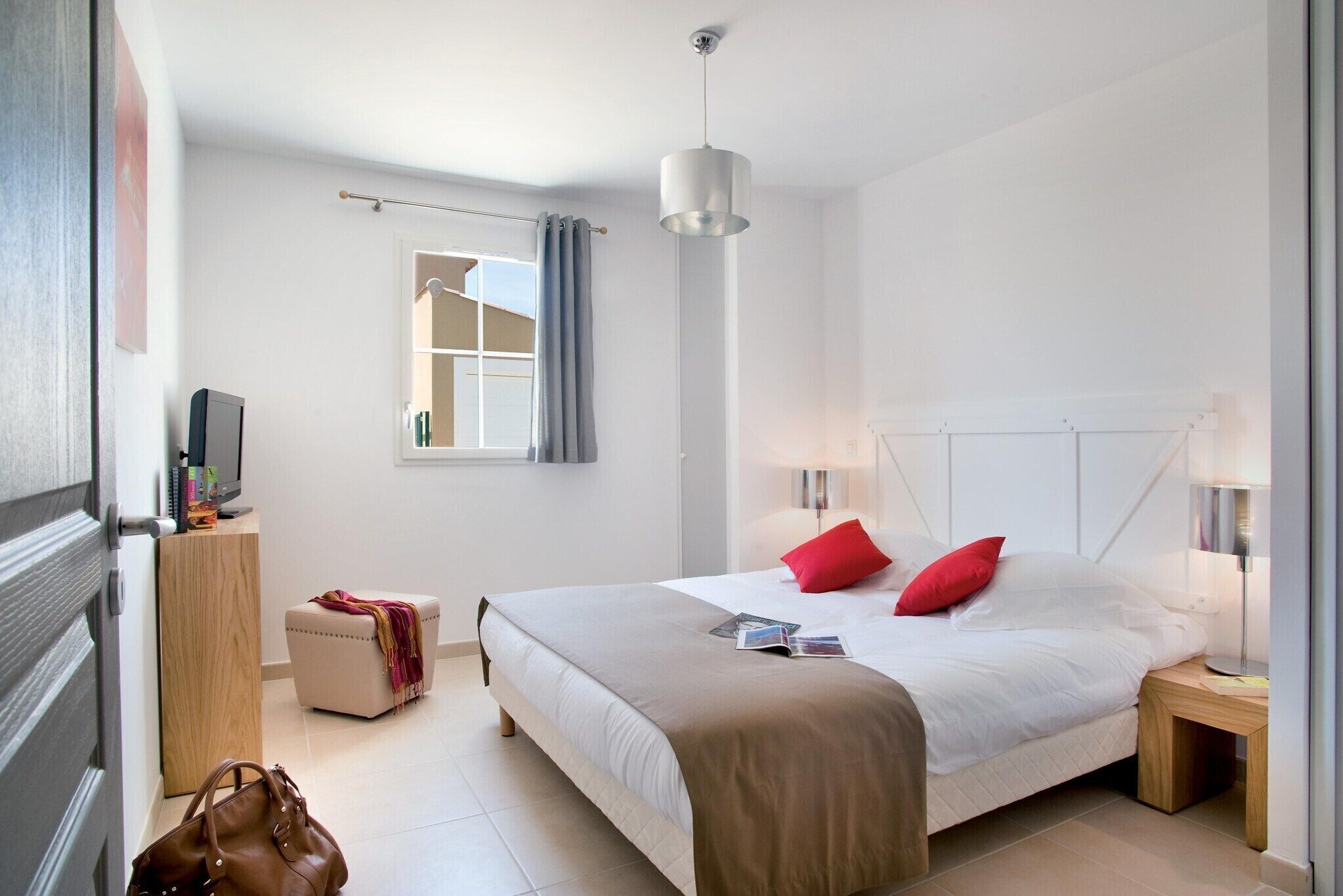Una habitació d'hotel amb un llit, taules de nit, un televisor, una finestra amb cortines i una porta.