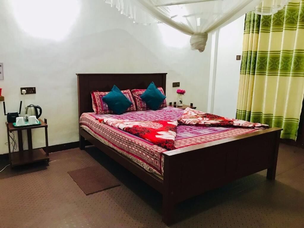 A bedroom with a bed, a bedside table, a nightstand, a lamp, and a window with curtains.