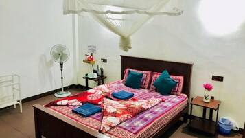 A bed with a canopy, a bedside table with a vase, and a standing fan.