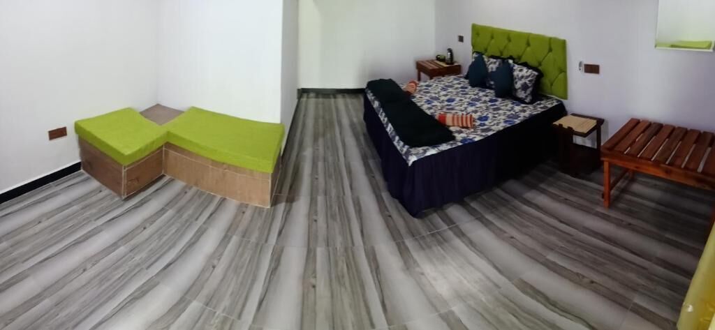 Un dormitorio con cama, mesita de noche, banco de madera y sofá verde.