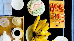 A breakfast tray with a teapot, cups, a plate of bananas, a fruit salad, and a slice of cake. - Helly mount inn (Ella)