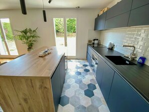 A modern kitchen with a wooden countertop, dark cabinets, a hexagonal tile floor, and a view through a glass door. - Renovated house in Courteuil near Chantilly (Courteuil)