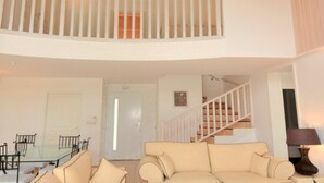En stue med et glasbord, en beige sofa, en trappe og et hvidt gelænder.