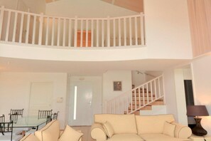 Ein Wohnzimmer mit einem Glastisch, einem beigen Sofa, einer Treppe und einem weißen Geländer.