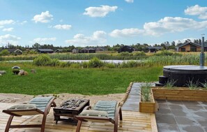 A wooden deck with lounge chairs and a table, a pond, and houses in the background. - Holiday home with hot tub near Ålbæk and Skagen (Jerup)