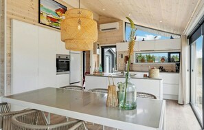 A modern kitchen with white cabinetry, a glass dining table, wicker chairs, and a hanging light fixture. - Holiday home with hot tub near Ålbæk and Skagen (Jerup)
