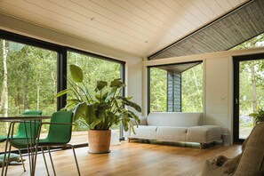 Interior moderno com piso de madeira, uma cadeira verde, um sofá bege e uma grande planta em vaso.