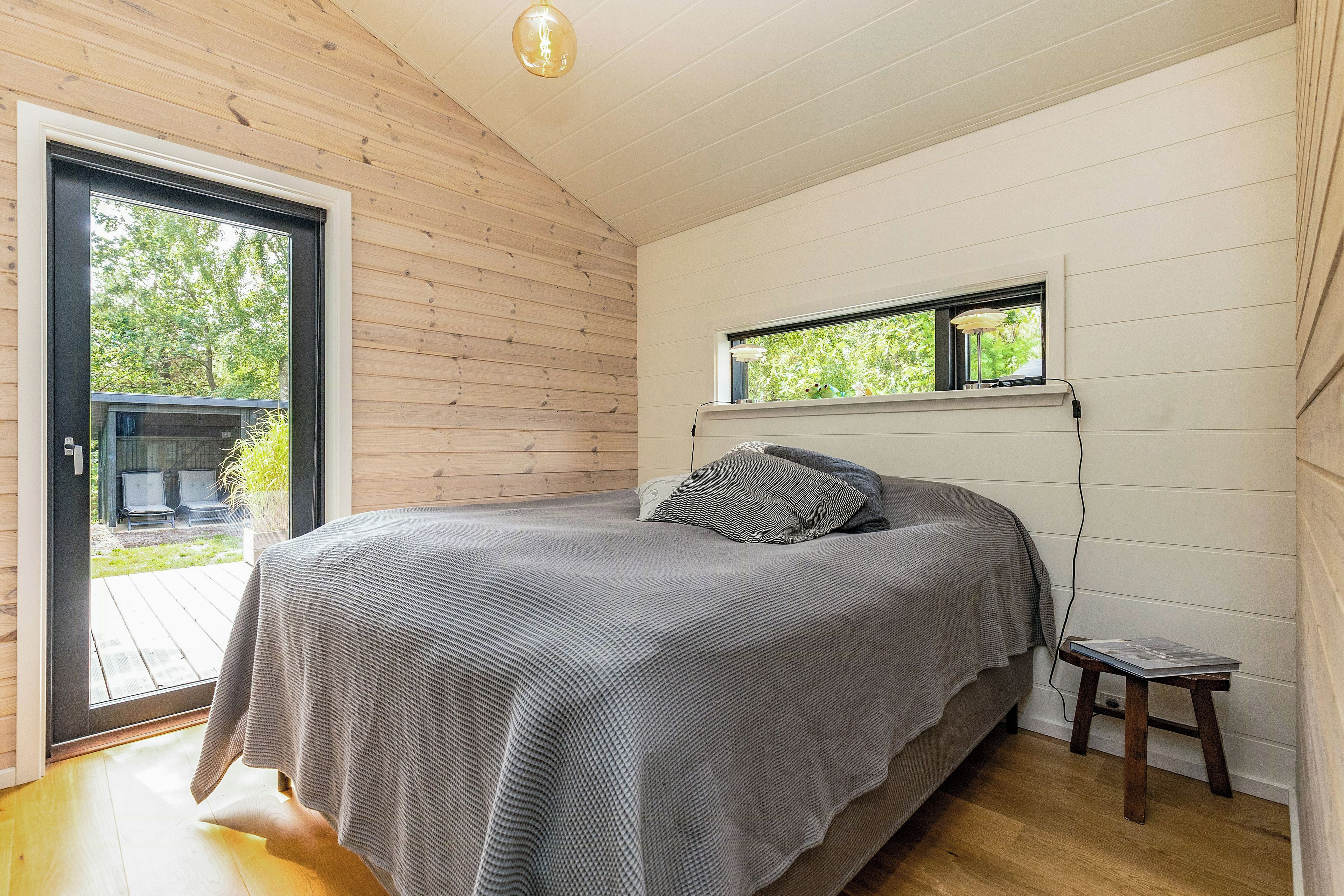 A bedroom with a bed, a window, a small table, and a view of the outdoors.