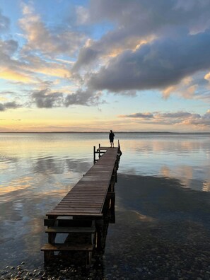Eine Holzstege, der sich in ruhiges Wasser erstreckt, mit einer Person am Ende.