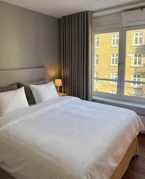 Une chambre d’hôtel avec un grand lit, une table de chevet, une lampe et une fenêtre donnant sur des immeubles.