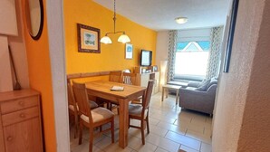 En matplats med ett träbord och stolar, en tv och en soffa i bakgrunden.
