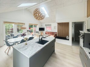 Eine moderne Küche mit einer Marmorinsel, ein Essbereich mit einem runden Tisch und ein Wohnbereich mit Sofa und Fernseher.