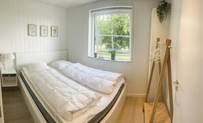 Ein Schlafzimmer mit zwei Einzelbetten, einem Fenster mit Blick auf Grünflächen, einem Nachttisch mit Lampe und einer Pflanze auf der Fensterbank.