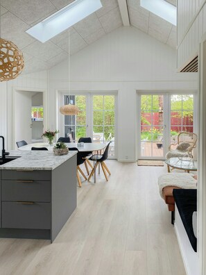 Eine moderne Küche mit Marmorarbeitsplatte, Holzboden und einem Essbereich mit Glastisch und Stühlen.