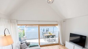 A modern living room with a sofa, a coffee table, a TV, and a balcony with a view.