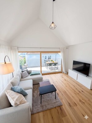 Ein modernes Wohnzimmer mit einer Couch, einem Couchtisch, einem Fernseher und einem Balkon mit Blick.
