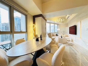 Ein modernes Hotelzimmer mit einem großen runden Tisch, bequemen Sitzgelegenheiten, einer Couch, einem Fernseher und großen Fenstern mit Blick auf die Stadt.