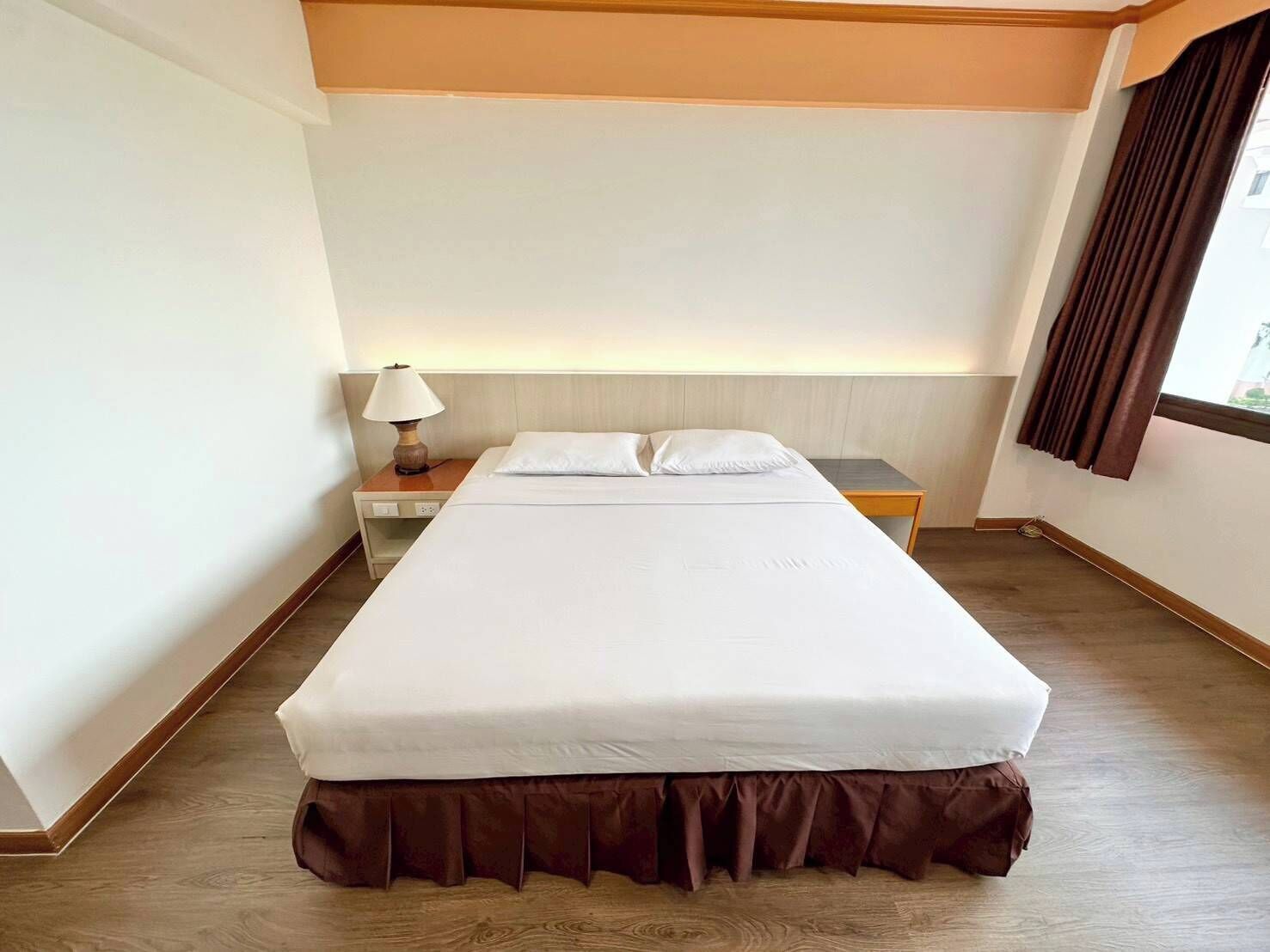 Une chambre d’hôtel avec un lit, une table de chevet, une lampe et une fenêtre avec des rideaux.