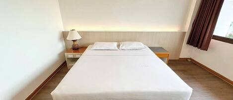 Une chambre d’hôtel avec un lit, une table de chevet, une lampe et une fenêtre avec des rideaux.