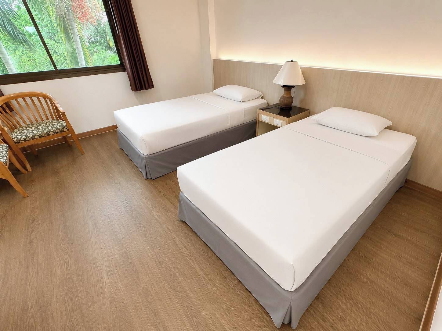 Hotelkamer met twee enkele bedden, een houten stoel, een nachtkastje met lamp en een raam met gordijnen.