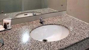 Casa de banho com lavatório em bancada de granito, cabine de duche em vidro e espelho.