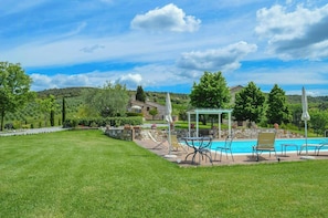 A pool area with lounge chairs and a gazebo, surrounded by a well-maintained lawn and stone walls. - Stone house apartment with pool in Tuscan hills (Asciano)