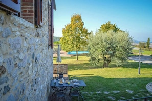 A stone wall, a table with plates, and a tree in a garden. - Stone house apartment with pool in Tuscan hills (Asciano)