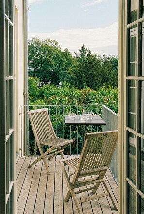 Une terrasse en bois avec deux chaises et une table, donnant sur un jardin agrémenté d’arbres et d’arbustes.