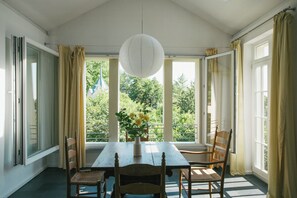 Ein Essbereich mit Tisch, Stühlen, einer Blumenvase und großen Fenstern mit Vorhängen.