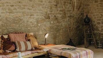 Una habitación rústica con pared de piedra, una cama de madera, una mesita pequeña y una escalera.