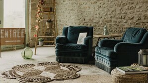A rustic room with a stone wall, a ladder with lights, two dark blue armchairs, a woven rug, and a small round table with a book. - Charming 1920s house in Picardy, 2h from Paris (Sainte-Croix)