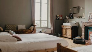 A bedroom with a large bed, a wooden dresser, a radiator, and a window with curtains. - Charming 1920s house in Picardy, 2h from Paris (Sainte-Croix)