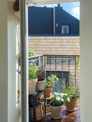 A view through a door into a patio area with potted plants, a metal shelf, and a brick wall. - Penthouse with private garden (København)