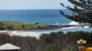 A coastal landscape with a beach, rocky shoreline, and vegetation. - Sandilands 1 - Lifestyle Yamba (YAMBA)