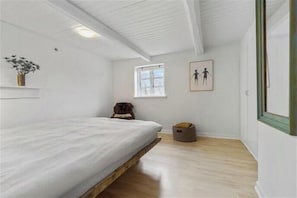 Ein Schlafzimmer mit einem Bett, einem Fenster, einer Wandpflanze, einem gerahmten Bild und einem kleinen Hundebett.