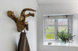 Ein Zimmer mit einer großen Holzskulptur an der Wand, einem Fenster mit Blick auf Grünflächen und einer Pflanzvase auf der Fensterbank.