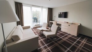 A hotel room with a sofa, two chairs, a small table, a TV, and a kitchen area.