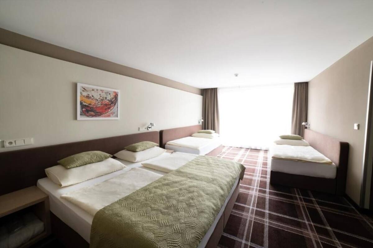 Habitación de hotel con tres camas, un ventanal grande y un cuadro en la pared.