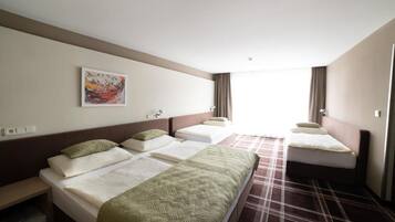 Habitación de hotel con tres camas, un ventanal grande y un cuadro en la pared.