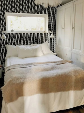 Un dormitorio con cama, paredes blancas, una ventana y un armario.